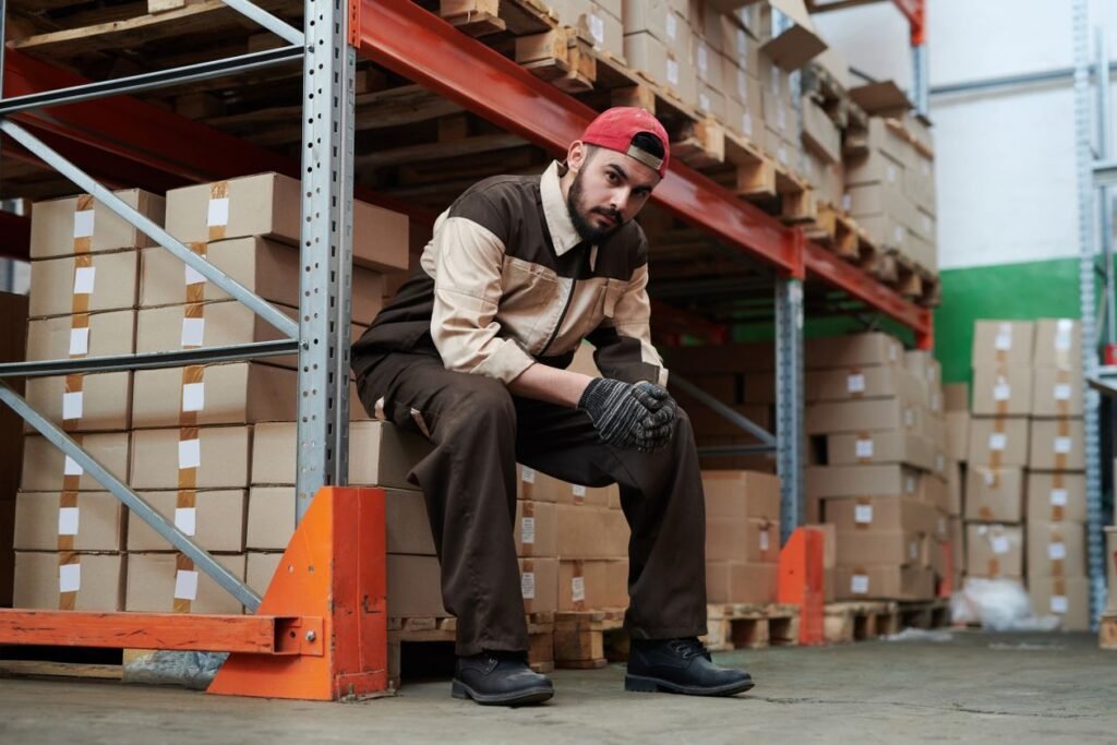 Warehouse worker sitting on a pallet between stocked shelves